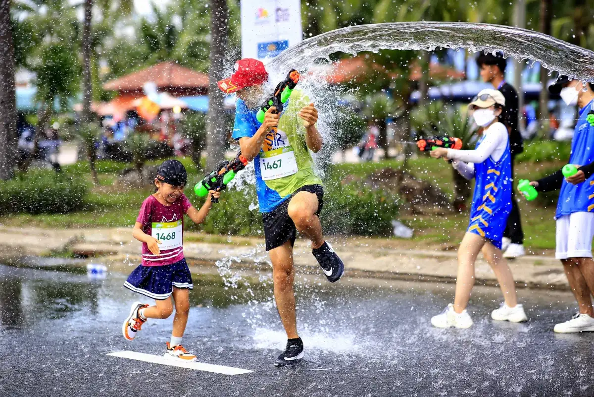 Children and runners wearing bibs splashing through a water spray at a family fun run